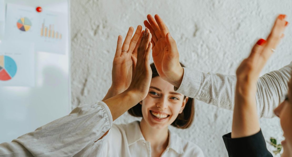 Quatre personnes se donnent des high-fives, souriant et partageant un moment de joie et d'optimisme au bureau.